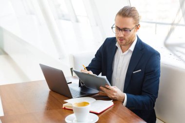 Ciddi bir genç iş adamının ofiste dizüstü bilgisayarla pano tutarken görüntüsü.