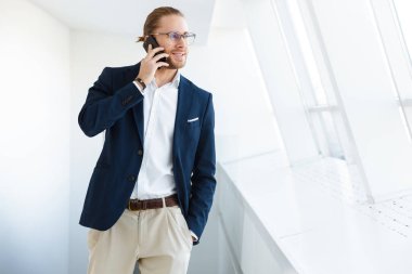 Ofiste cep telefonuyla konuşan yakışıklı, pozitif memnun genç iş adamının görüntüsü.