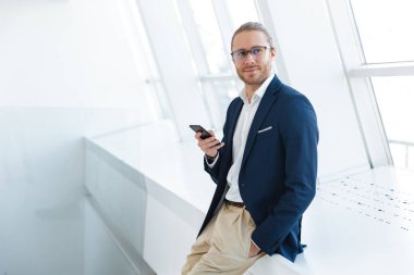 Ofiste cep telefonu kullanan yakışıklı, pozitif memnun genç iş adamının görüntüsü.