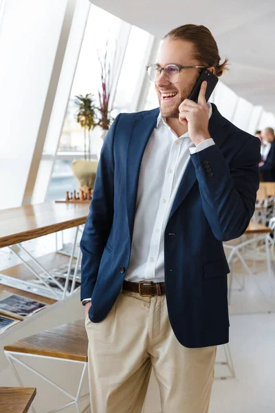 一个英俊的 积极的 快乐的年轻商人在办公室里用手机交谈的照片 — 图库照片
