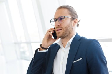 Ofiste cep telefonuyla konuşan ciddi konsantre genç iş adamının görüntüsü.