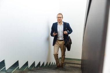 Yakışıklı, memnun genç iş adamının görüntüsü. Üst katta cep telefonuyla yürüyor..