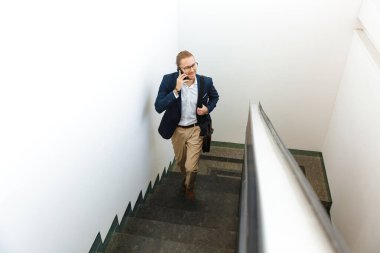 Yakışıklı, mutlu, genç iş adamının resmi. Üst katta cep telefonuyla konuşuyor..