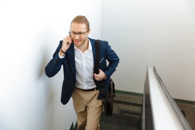 Yakışıklı memnun genç iş adamının resmi. Üst katta cep telefonuyla konuşuyor..