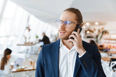 Ofiste cep telefonuyla konuşan yakışıklı, ciddi, konsantre genç iş adamının görüntüsü.