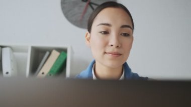Ofiste çalışırken bilgisayarını kullanan genç ve güzel bir Asyalı sekreterin görüntüsü.