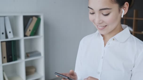 Pěkná Mladá Asijská Sekretářka Žena Bezdrátovými Sluchátky Pomocí Svého Mobilního — Stock video