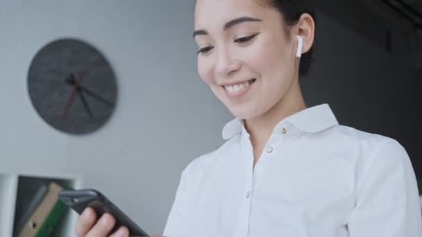 Una Joven Mujer Negocios Asiática Sonriente Con Auriculares Inalámbricos Está — Vídeos de Stock