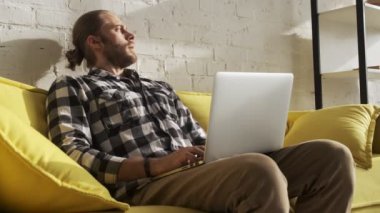 Sakin bir adam evdeki oturma odasında laptopuyla çalışıyor.
