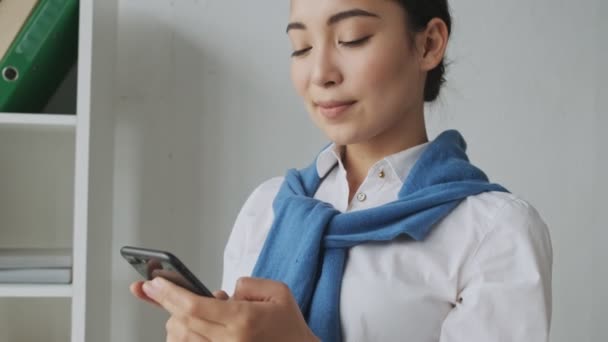 Uśmiechnięta Młoda Azjatycka Sekretarka Pisze Wiadomość Przez Telefon Komórkowy Siedząc — Wideo stockowe