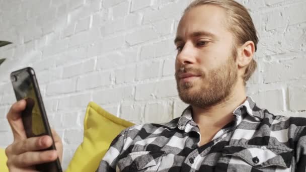 Ein Zufriedener Mann Sitzt Mit Seinem Smartphone Heimischen Wohnzimmer — Stockvideo