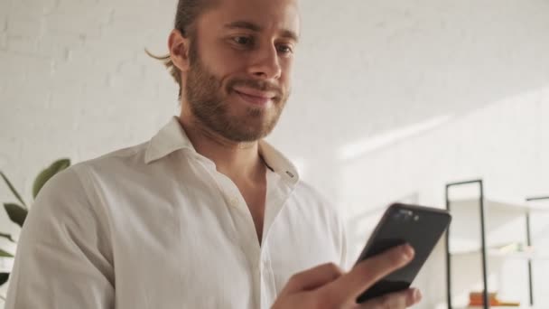 Yakışıklı Bir Adam Akıllı Telefonunu Evdeki Oturma Odasında Kullanıyor — Stok video