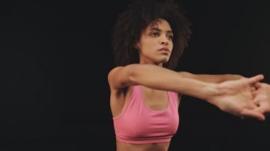 Spor giyimli sakin bir Afrikalı Amerikalı kadın siyah arka planda izole edilmiş spor egzersizleri yapıyor.