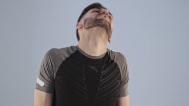 Spor kıyafetli genç bir sporcu boynu ısınırken stüdyoda gri arka planda çalışıyor.