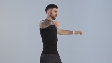 Spor kıyafetleri içinde odaklanmış genç bir sporcu stüdyodaki gri arka planda izole edilmiş ısınma egzersizleri yapıyor.