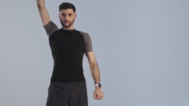 一位穿着运动服的强壮而专注的年轻运动员正在进行热身运动 他的胳膊被隔离在工作室的灰色背景之外进行着热身运动 — 图库视频影像