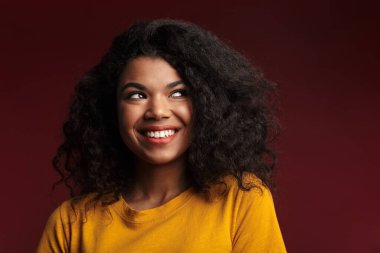 Kızıl arka planda izole edilmiş kameraya gülümseyen kıvırcık saçlı güzel esmer Afrikalı Amerikalı kadın.