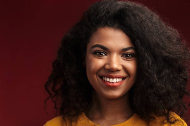 Kızıl arka planda izole edilmiş kameraya gülümseyen kıvırcık saçlı güzel esmer Afrikalı Amerikalı kadın.
