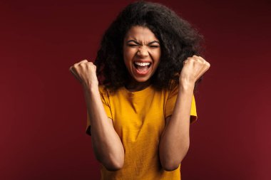 Güzel esmer Afro-Amerikalı kadın görüntüsü. Kıvırcık saçlı, neşeli ve yumruklarını kırmızı arka planda tutarak.