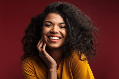Kızıl arka planda izole edilmiş kameraya gülümseyen kıvırcık saçlı güzel esmer Afrikalı Amerikalı kadın.