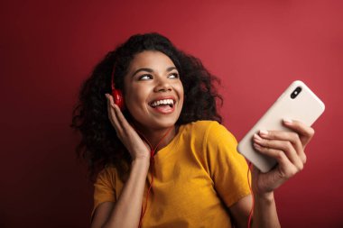 Güzel, esmer, Afro-Amerikalı bir kadının kırmızı arka planda şarkı söyleyip cep telefonu tutarken görüntüsü.