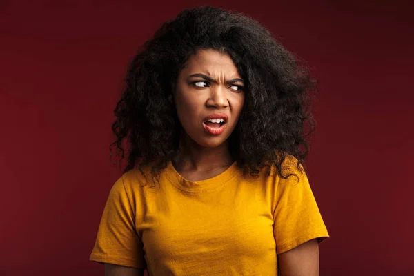 Image of angry displeased young african woman posing isolated over dark red wall background.