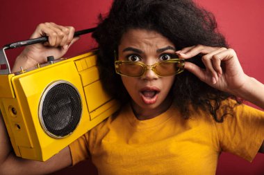 Kırmızı arka planda izole edilmiş, kıvırcık saçlı, esmer, Afro-Amerikalı bir kadının görüntüsü.