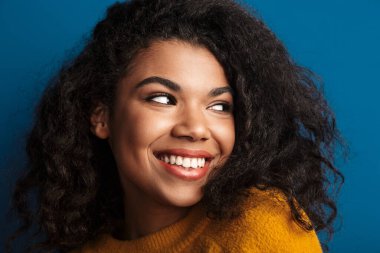 Mavi duvar arkasında izole edilmiş poz veren oldukça mutlu, iyimser, genç bir Afrikalı kadın..