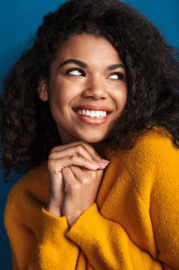 Güzel gülümseyen, iyimser, genç bir Afrikalı kadının mavi duvar arkasında izole poz verirken çekilmiş fotoğrafı..