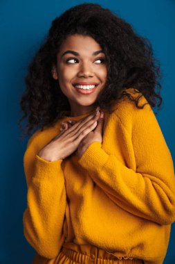 Mavi duvar arkasında izole edilmiş poz veren oldukça mutlu, iyimser, genç bir Afrikalı kadın..