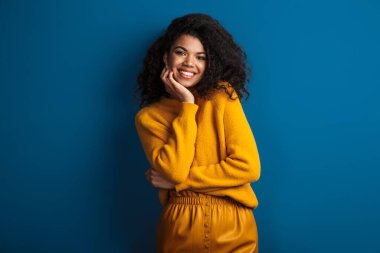 Güzel gülümseyen, iyimser, genç bir Afrikalı kadının mavi duvar arkasında izole poz verirken çekilmiş fotoğrafı..