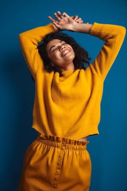 Mavi duvar arkasında izole edilmiş poz veren oldukça mutlu, iyimser, genç bir Afrikalı kadın..