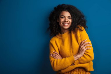 Mavi duvar arkasında izole edilmiş poz veren oldukça neşeli, iyimser bir Afrikalı kadının görüntüsü..