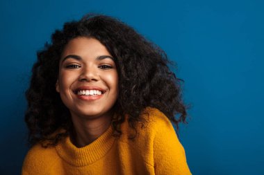 Güzel gülümseyen, iyimser, genç bir Afrikalı kadının mavi duvar arkasında izole poz verirken çekilmiş fotoğrafı..