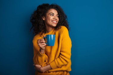 Neşeli, mutlu, duygusal, Afrikalı bir kadının mavi duvar arkasında izole bir şekilde çay içerken görüntüsü..
