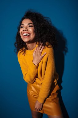 Mavi duvar arkasında izole edilmiş poz veren neşeli, gülen Afrikalı genç bir kadının fotoğrafı..