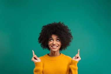 Yeşil arka planda tek başına dikilip fotokopi alanını gösteren gülümseyen Afrikalı genç bir kadının portresi.