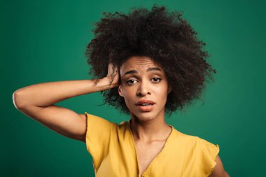 Kafası karışmış genç bir Afrikalı kadının portresi yeşil arka planda tek başına duruyor.