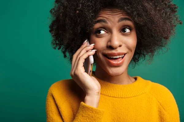 一个笑着的年轻非洲女人的画像 她穿着毛衣 孤零零地站在绿色的背景上 在手机上聊天 — 图库照片