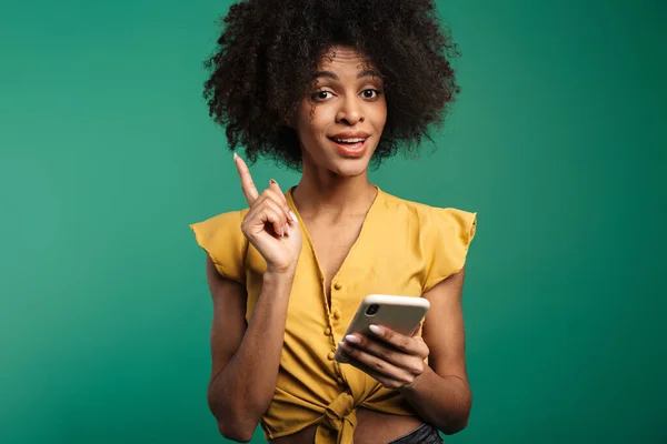 携帯電話を使って緑の背景に隔離された幸せな若いアフリカ人女性の肖像画 — ストック写真