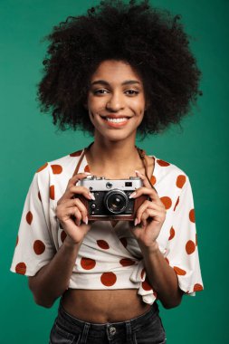 Pozitif Afrikalı kıvırcık kadın fotoğrafçı görüntüsü. Koyu mavi duvar arkasında kamera ile izole edilmiş poz veren bir turist..