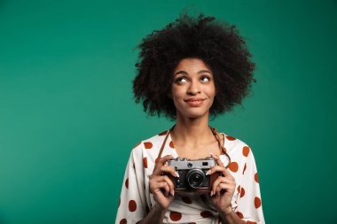 Rüya gören Afrikalı kıvırcık kadın fotoğrafçının fotoğrafı. Koyu mavi duvar arka planında kamera ile izole edilmiş poz veren bir fotoğrafçı..