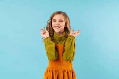 Mavi arka planda saklanmış, parmaklarını çapraz yapıp gülümseyen komik sarışın kızın fotoğrafı.