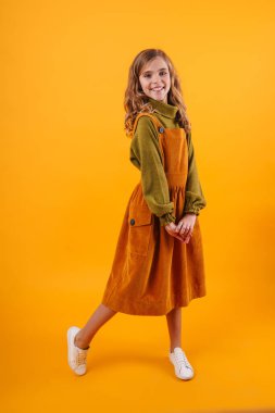 Mavi arka planda tek başına duran, elbise giyen gülümseyen küçük bir kız.