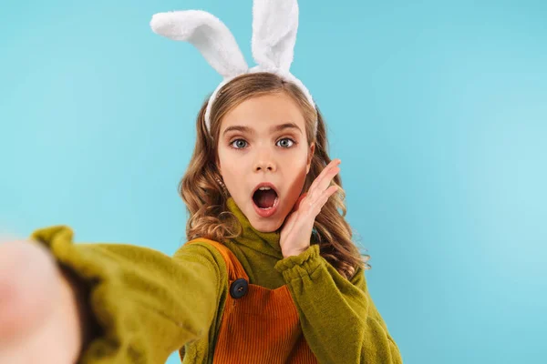 おもちゃのウサギの耳で興奮したブロンドの女の子の写真撮影自画撮りと表現驚き隔離された上の青の背景 — ストック写真