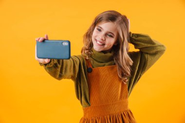 Mutlu, güzel bir kızın cep telefonuyla selfie çektiği ve mavi arka planda izole bir şekilde gülümsediği fotoğraf.