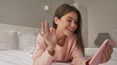 Mutlu, genç ve çekici bir kız, akıllı telefonunu kullanarak evde ve yatakta bir video görüşmesi yapıyor.