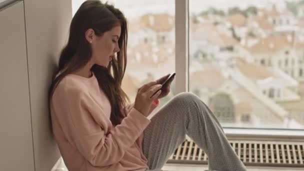 Piękna Dziewczyna Używa Swojego Smartfona Siedząc Rano Przy Oknie Domu — Wideo stockowe