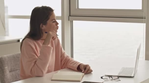 Привлекательная Девушка Пишет Блокноте Используя Свой Ноутбук Сидя Столом Кухне — стоковое видео