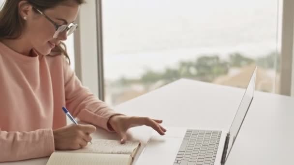 Una Chica Sonriente Con Gafas Está Escribiendo Algo Cuaderno Usando — Vídeos de Stock